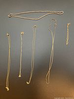 Six slender gold necklaces and one twisted rope gold chain laid out on black background