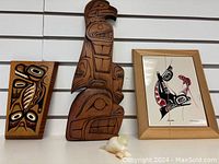 Three Indigenous art pieces including the wood sculptures of eagle and bear, the ceramic tile artwork framed print 'Survival' by DM Dennis, and a small ivory or bone carving.