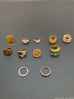 Overview of all eleven gold-colored ladies rings arranged on dark surface