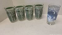 Set of 5 highball glasses displayed: 4 green with white Egyptian motifs and 1 blue with white decorative scene.
