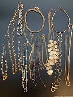 Photo showing a variety of gold coloured necklaces ranging from beaded necklaces, linked rings, coin pendant chains and mixed styles laid out on a dark background.