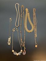Lot showing all six gold-colored necklaces arranged on flat surface, various chain styles and pendants visible.