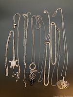 Eight silver coloured necklaces arranged on a flat surface showing a variety of pendants and chain styles.