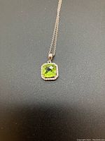 Pendant and part of chain on dark background, showing peridot's color and diamond halo.