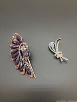 Two accessories on gray background: large purple stone hair clip and small silver-tone rhinestone brooch