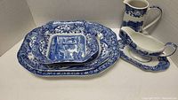 Overview of two large platters stacked under square serving dish, pitcher and gravy boat