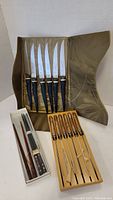 Photo showing a box set of six vintage Sheffield steak cutters with dark bone handles and stainless steel blades, next to two sets of lacquer chopsticks in plastic boxes.