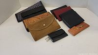 Top view showing collection of wallets: tan suede, embossed floral leather, black leather, fabric wallet, red and black wallets, and small orange embossed leather key holder.