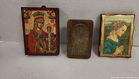 Set of three wood block religious icons, two hand-painted and one engraved metal, shown side by side.