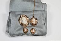 Full view of the cameo jewelry set including brooch, pendant and earrings laid on gray fabric showing the ornate designs and colors.
