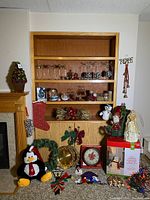 Wide view of the Christmas decorations arranged on and around wooden shelving and floor, showing ornaments, wreaths, plush toys and boxed snowman, stocking, and lights.