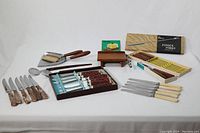 Wide angle photo showing all utensil items including boxed fondu forks, cheese slicer, nutcracker, bone handled knives, and other wooden-handled cutting utensils.