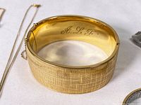 Front view of gold filled bangle showing textured surface and safety chain on white background.
