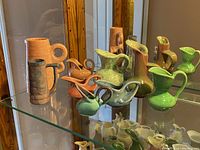 Glass shelf holding a variety of nine pastel solid color ceramic jugs of multiple shapes and sizes