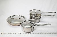 Full set of KitchenAid stainless steel pots and pans showing four pieces with lids on a white background with measuring tape for scale.