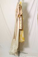 Side view of four hanging dresses and top, showing length and fabrics in neutral and metallic tones