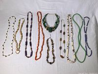 Full view of 10 gemstone necklaces laid out side by side on white background showing variety of colors and bead shapes.