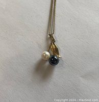 Pendant front view showing white and dark pearls and gold leaf design on chain