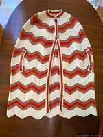Full top-view photo of the hand crocheted poncho laid flat, showing chevron pattern in cream, orange, and brown, with button closure and slip pockets.