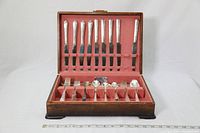 Open wooden cutlery box showing organized sets of silverplate cutlery including knives, forks, and spoons with pink velvet lining.