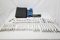 Full assortment of spoons displayed on table, including storage cases and cloth rolls in background, showing quantity and variety.