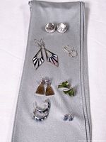 Seven pairs of sterling silver earrings arranged on a gray cloth showing different shapes and styles including pierced and screw-on types.