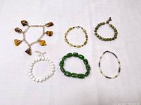 Full view of six stone bracelets laid on white background, showing variety including tiger eye charm bracelet and jade bead bracelet.