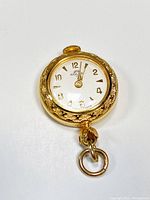 Front view of gold tone round pendant watch showing white dial with gold Arabic numerals and hands, marked Solar and Swiss Made.
