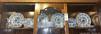 Full display of Adams England blue and white dish set with glass stemware in wooden cabinet.