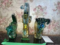 Front view of three colored glass animal paperweights: raccoon, elephant, yak