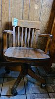 Front view of a solid wood bankers desk chair with slatted back and wooden armrests. Chair shows some paint spatter and wear on the finish.