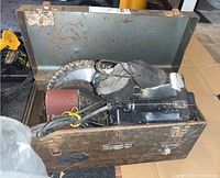 Open rusty Mastercraft metal toolbox showing contents including sanding belts, circular saw blade, and Black and Decker belt sander with power cord and dust bag.