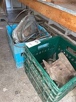 Blue plastic crate containing large metal pulley block and thick steel cable coiled around it, positioned next to a heavy cast iron rail approximately 13 inches long.