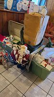 Photo shows two large plastic storage totes with lids containing assorted Christmas decorations, standing Santa and reindeer figures in front, tall boxed tree behind them.