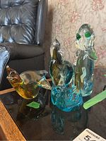 Photo showing the four coloured glass animal paperweights on a glass table, including a dog, bird, mouse chalet, and owl.