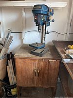 Mastercraft drill press on the wooden cabinet, showing the full setup including the cabinet base and drill press body with adjustable table.