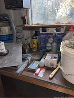 Photo showing workbench with bucket and masonry trowels, radial shock absorber packaging, various small tools and workshop supplies.