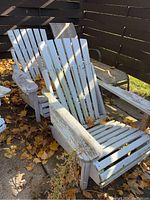 Two white painted wooden Muskoka chairs with visible wear and dirt, placed outside on concrete with fallen autumn leaves.
