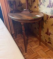 Full view of the wooden oval side table from the front next to a couch and floral wallpaper background showing table legs and wood grain.