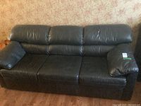 Front view of black leather three-seater sofa showing full seating area, backrest cushions, and armrests.