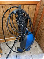 Full view of Simonize blue and black power washer with coiled hose and wand, showing unit on wheels and attached hose.