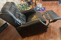 Black reclining armchair with button-tufted backrest and footrest extended, upholstered in synthetic leather with visible wear.