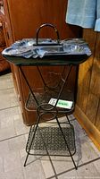 Front view of the ceramic ashtray top on black wire stand with two wire shelves, showing the scalloped edges and handle on ashtray.