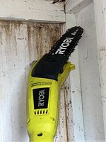 Yellow and black Ryobi cutting head with 8" chain bar attached, mounted on white shed wall