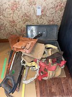Overview showing saws, tool belts, toolbox on floor against floral wallpaper background