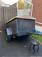 Rear view of the black plywood utility trailer with hinged roof closed, showing hitch and one flat tire.