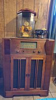 Front view of Garrard record player cabinet showing wooden case, speaker doors, and control knobs on front. Top has glass cover with decorative items inside.
