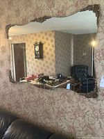 Front view of large wall mirror mounted on floral wallpapered wall reflecting room interior.