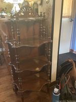 Front and angled view of dark wooden what not shelf showcasing three scalloped shelves, turned legs, and carved back splash.