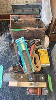Photo of wooden and metal toolboxes with various hand tools including wood planes, rasps, and file in packaging arranged on floor.